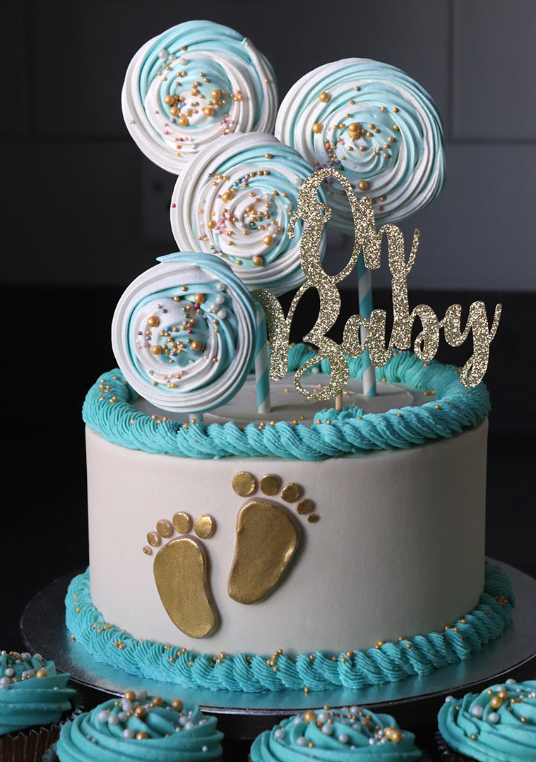 A gluten-free, lactose-free vanilla cake for a baby shower. Layered with vanilla buttercream and decorated with piped swirls and meringue lollipops. All made with glutenfree, lactosefree ingredients. Also in the picture: vegan chocolate cupcakes. Delivered in London