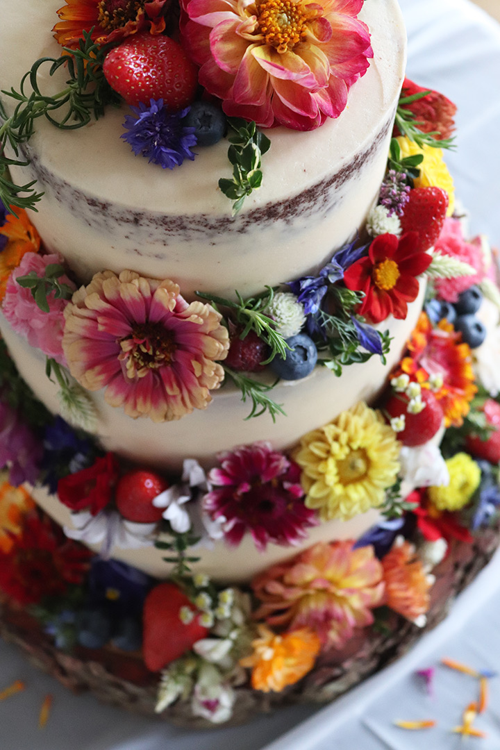 A semi-nude gluten free July wedding cake at London Rowing Club. Three tiers of layered Chocolate & Olive Oil Cake. All ingredients glutenfree, lactosefree, soyafree, nutfree. Decorated with fabulous flowers, all organic and edible, from Aweside Farm. Price includes delivery and assembly at your London venue