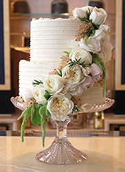 The perfect centrepiece for your glutenfree wedding: a two-tier white wedding cake for a summer wedding at the Belmond Cadogan Hotel. Gluten-free, wheat-free and milk-free. Two tiers of award-winning dairyfree Tunisian Orange & Almond Cake, filled and frosted with dairy-free lemon buttercream. All ingredients gluten free and milk free. Price includes tasting consultation, and delivery and assembly at your London venue. Organic edible roses from Maddocks Farm Organics