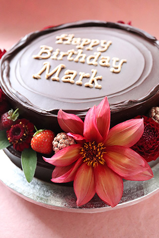 A gluten-free stacked chocolate cake, made with chocolate, almonds and rum. Covered with dark ganache and decorated with fresh berries and organic edible flowers. All made with glutenfree ingredients, and delivered in London
