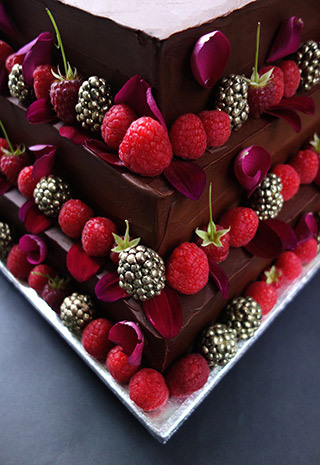 Glutenfree rich chocolate & rum birthday cake. A 3-tier, stacked Reine de Saba, decorated with raspberries, rose petals and gilded blackberries. All ingredients gluten free