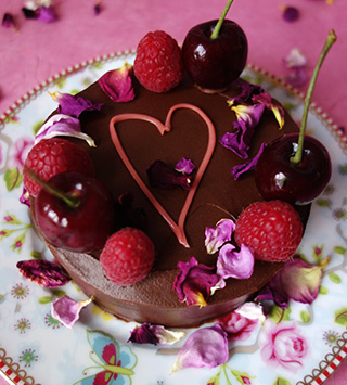 Award-winning gluten free rich mini chocolate cake made with organic ground almonds and dark chocolate, and Jamaica Rum. Covered with dark chocolate ganache and decorated with piped pink heart in organic white chocolate, cherries, berries & edible rose petals. All ingredients glutenfree. Available diary free