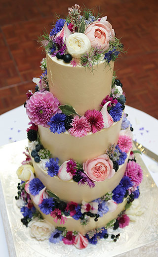 A gorgeous four-tier summer wedding cake. Three tiers of gluten-free White Chocolate cake and a bottom tier of gluten-free, dairy-free Chocolate & Olive Oil Cake. Filled and frosted with white chocolate Swiss meringue buttercream, and decorated with organic edible flowers, fresh blackcurrants and raspberry meringue kisses. All ingredients gluten free. Price includes tasting consultation, and delivery and assembly at your London venue. Organic edible flowers from maddocksfarmorganics.co.uk